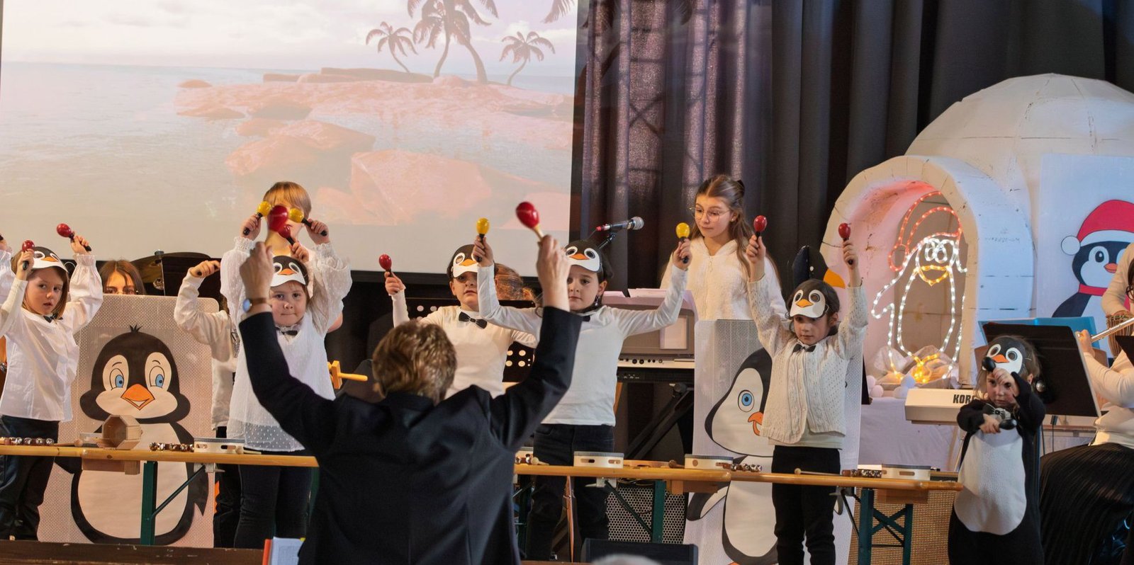 Les enfants en costume de pingouin jouant des maracas sur scène